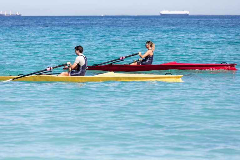 Zwei Ruderer in gelben und roten Coastal Booten (X-Adventure) rudern im türkisfarbenen Wasser.